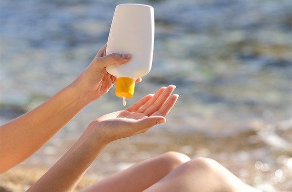 person squeezing sunscreen at the beach