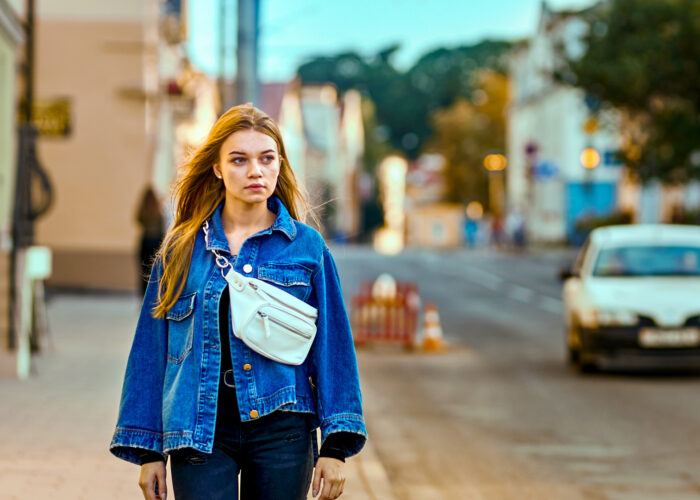 girl in a denim jacket and waist bag walks through the city along the road