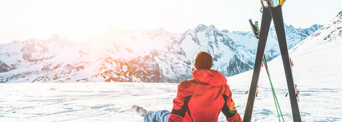 Man sitting next to ski poles looking at mountains