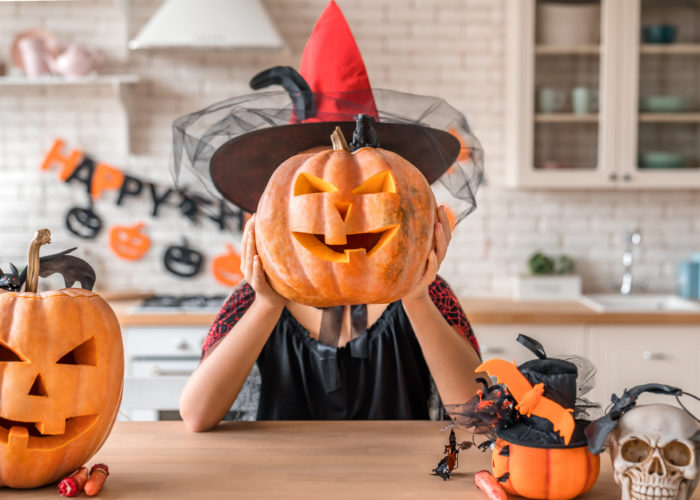 Woman dressed as a witch holding a jack-o-lantern in front of her face