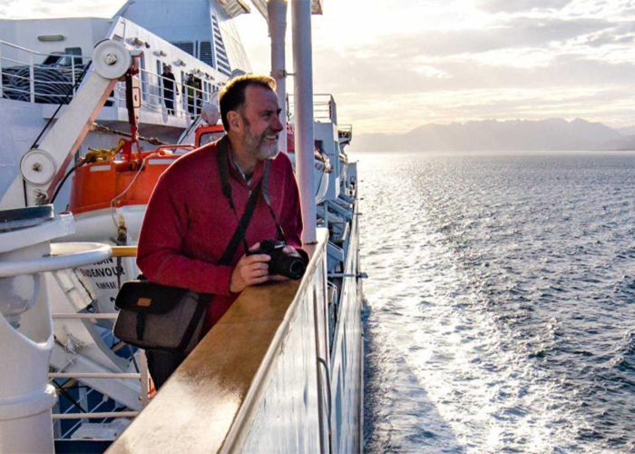 Man holds camera, leaning over railing of ship in Antarctica