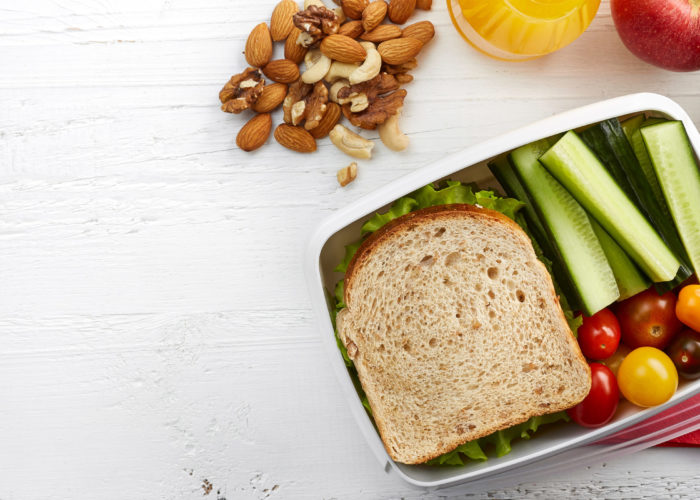 Flat lay of a packed lunch with a sandwich, nuts, fruit, vegetables, and a bottle of orange juice