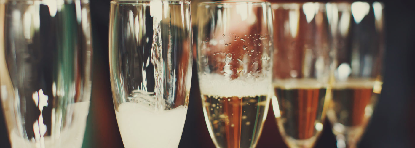 Close up of row of champagne glasses being filled by a bottle