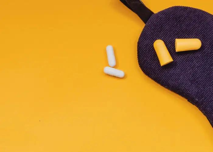Sleep mask, eargplugs, and sleeping pills on yellow background