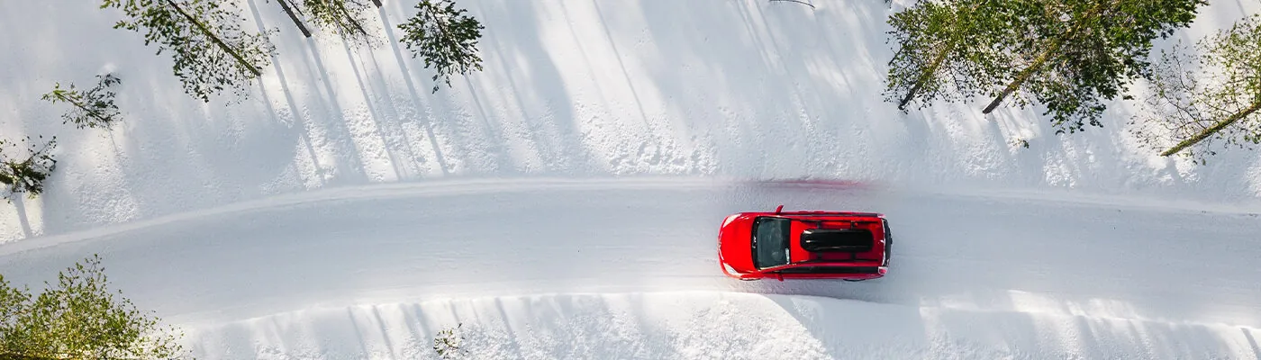 Aerial view of red car driving through snowy forest