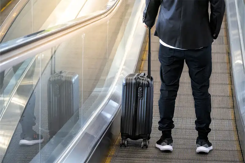 Man with rolling suitcase on moving walkway