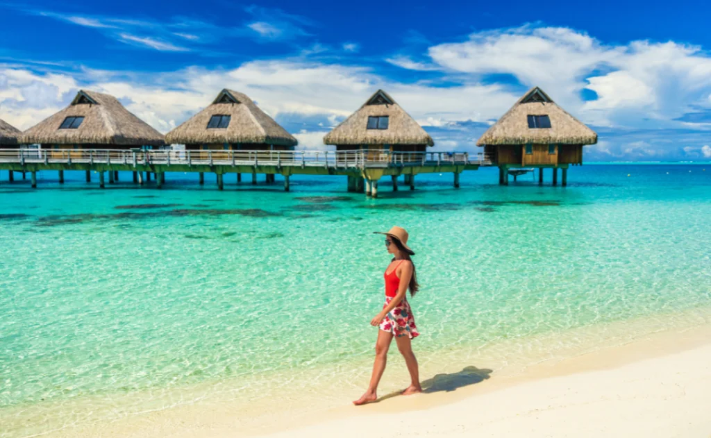 Beach vacation woman walking on Bora Bora beach in Tahiti, French Polynesia at luxury overwater bungalows hotels honeymoon destination